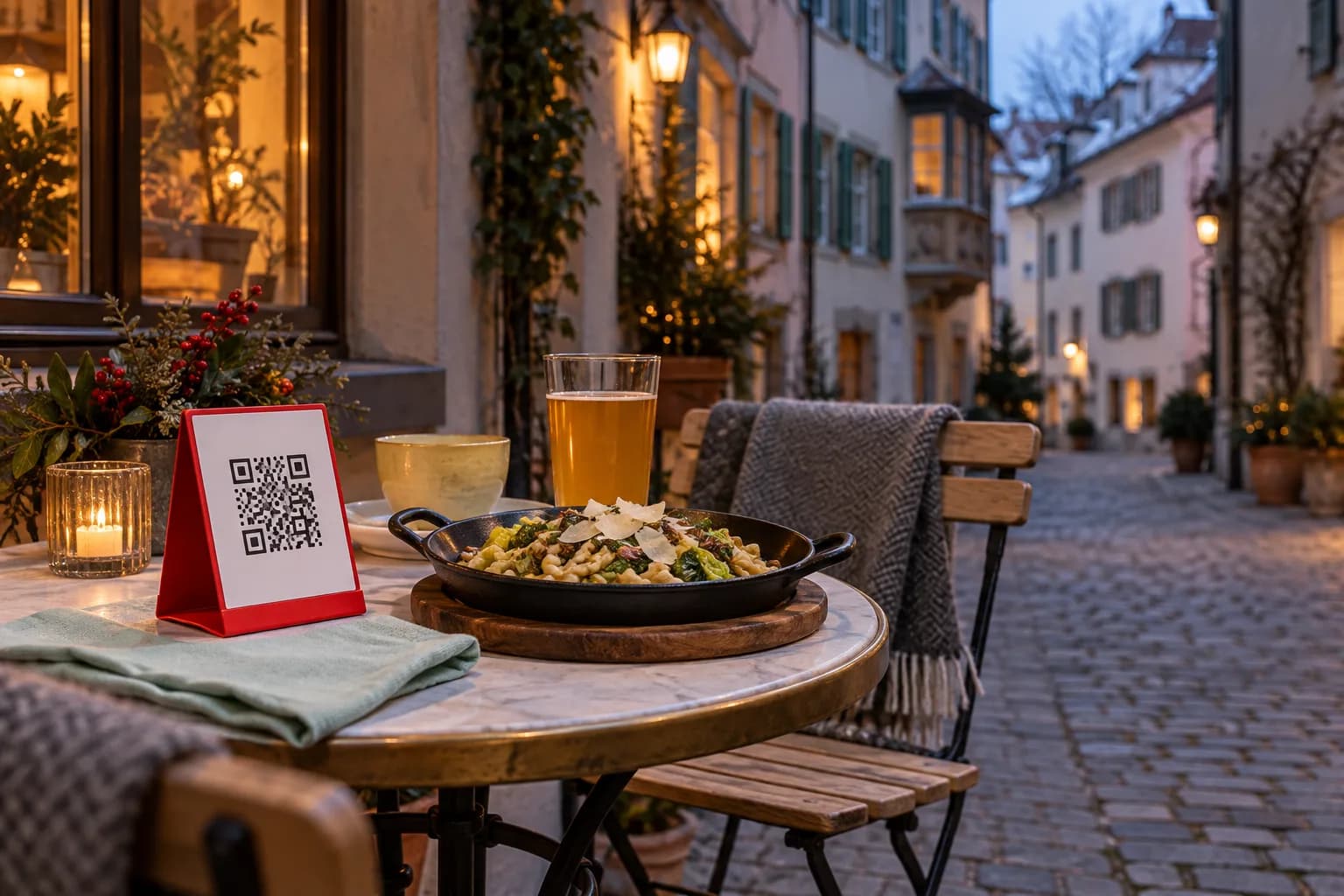 Table de café dans une ruelle de la vieille ville de Zurich un soir d’hiver, avec un chevalet de QR code rouge, des Pizokel au chou et un verre de kombucha